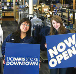 Photo: Two student employees holding signs that read UC Davis Store Downtown and Now Open