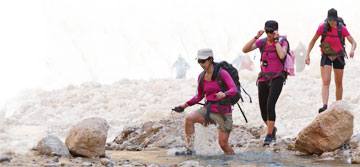 Photo: Three UC Davis alumna cross stream in hiking gear and carrying backpacks