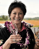 Photo: woman, smiling, holding empty wine glasses, wearing a Hawaiian shirt and lei