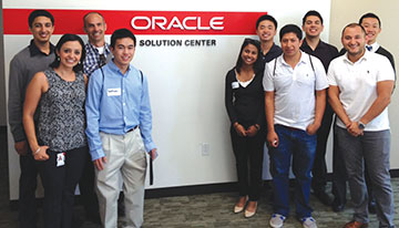 Smiling group standing in front of interior wall with sign that reads Oracle Solution Center