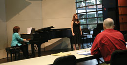 Photo: audition room scene with female singer, pianist and judge
