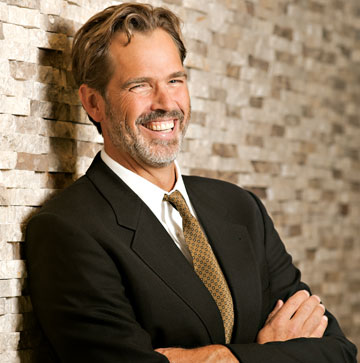 Photo: smiling professor, leaning against stone wall