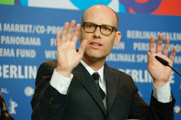 The director with both hands up, sitting in from of Berlin film fest banner