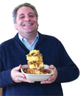 Photo: smiling man holding bowl piled with corn bread and chile