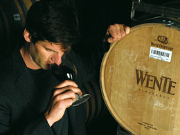 Photo: winemaker sniffing a glass of red wine, hand resting on wine cask
